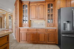 Kitchen with light stone counters, decorative backsplash, and stainless steel fridge with ice dispenser