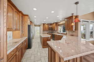 Kitchen featuring decorative light fixtures, stainless steel appliances, kitchen peninsula, a center island, and light stone countertops