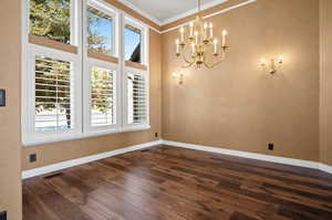 Spare room featuring ornamental molding, dark wood-type flooring, and an inviting chandelier