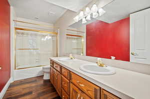 Full bathroom with toilet, hardwood / wood-style floors, vanity, a textured ceiling, and enclosed tub / shower combo