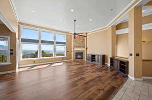 Unfurnished living room with ceiling fan, ornamental molding, a stone fireplace, and light wood-type flooring