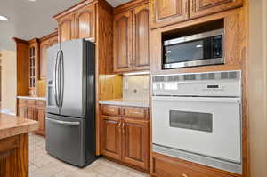 Kitchen with appliances with stainless steel finishes, tasteful backsplash, light stone counters, and light tile patterned floors