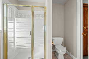 Bathroom with toilet, an enclosed shower, and tile patterned flooring