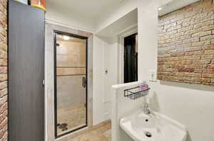 Bathroom with a shower with door, brick wall, and tile patterned floors