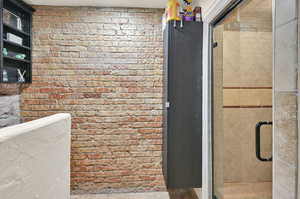 Bathroom featuring a shower with shower door and brick wall