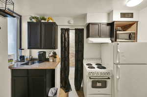 Kitchen featuring sink, light tile patterned floors, white appliances, and dark brown cabinets