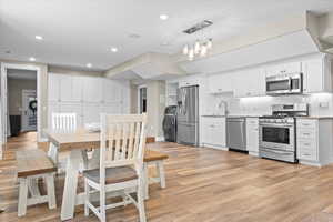 Basement Kitchen with light wood-type flooring, decorative light fixtures, stainless steel appliances, washer / dryer, and white cabinets