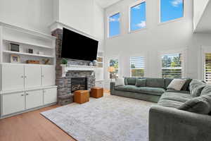 Living room featuring a towering ceiling, built in shelves, a fireplace, and light hardwood / wood-style flooring