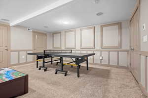 Recreation room featuring beamed ceiling, light carpet, and a textured ceiling