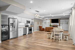 Basement kitchen with a large fireplace, white cabinetry, light hardwood / wood-style flooring, appliances with stainless steel finishes, and washer / clothes dryer