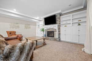 Living room featuring crown molding, light colored carpet, a stone fireplace, and built in shelves