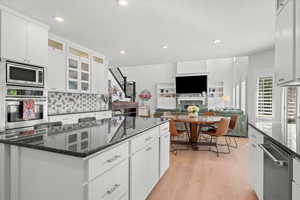 Kitchen with white cabinets, appliances with stainless steel finishes, a kitchen island, and light hardwood / wood-style floors