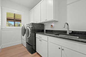 Clothes washing area featuring light hardwood / wood-style floors, sink, cabinets, and separate washer and dryer