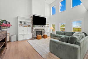 Living room with built in shelves, a high ceiling, a stone fireplace, and light wood-type flooring