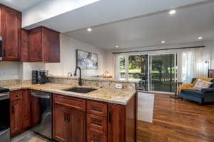 Kitchen with hardwood / wood-style floors, light stone counters, stainless steel appliances, sink, and kitchen peninsula