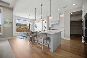 Kitchen with decorative light fixtures, white cabinets, a kitchen island with sink, and light hardwood / wood-style flooring