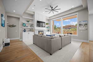 Living room featuring built in shelves, ceiling fan, light wood-type flooring, and a fireplace