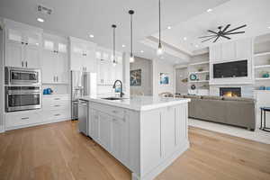 Kitchen featuring pendant lighting, an island with sink, ceiling fan, a stone fireplace, and appliances with stainless steel finishes