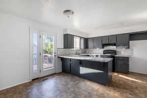 Kitchen featuring a textured ceiling, black / electric stove, kitchen peninsula, gray cabinets, and decorative backsplash