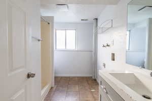 Bathroom with a textured ceiling, vanity, a shower, and tile patterned floors