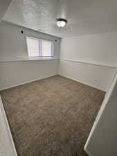 Unfurnished room featuring dark colored carpet and a textured ceiling