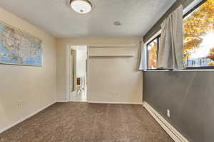 Unfurnished bedroom with a textured ceiling, carpet floors, a closet, and a baseboard heating unit