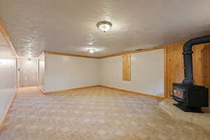 Basement featuring a wood stove, a textured ceiling, crown molding, and light colored carpet