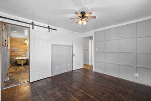 Primary bedroom with ceiling fan, connected bathroom, dark hardwood floors, and a barn door