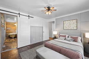 Bedroom with wood walls, ceiling fan, dark hardwood / wood-style floors, and a barn door