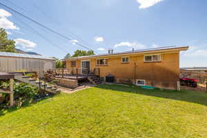 Rear view of house featuring central AC unit, a deck, and a lawn