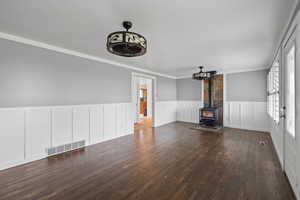 Unfurnished living room with ornamental molding, a wood stove, and dark hardwood / wood-style floors