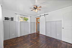 Primary bedroom with ceiling fan, ornamental molding, dark hardwood flooring, and a barn door