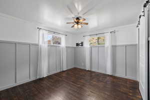 Primary bedroom with ceiling fan, a barn door, and dark hardwood flooring