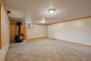 Basement featuring light colored carpet, a textured ceiling, wooden walls, and a wood stove