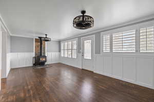 Foyer entrance with ornamental molding, dark wood-type flooring, and a wood stove