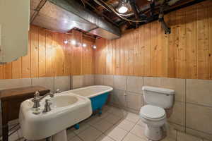 Bathroom with a bathtub, tile patterned flooring, wooden walls, and toilet