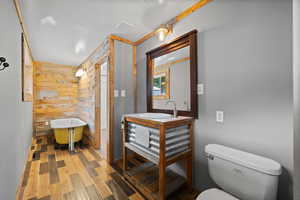 Primary bathroom featuring rustic vanity, wood-type flooring, a bath, wooden walls, and toilet