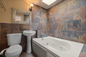 Bathroom featuring tile walls, a skylight, a bath, and toilet