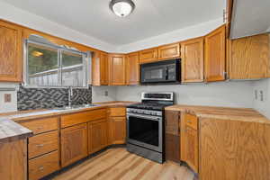 Kitchen with sink, butcher block counters, gas range, light LVP floors, and backsplash