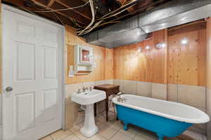 Bathroom featuring wooden walls, tile patterned flooring, and a bath