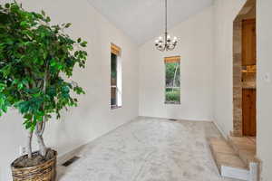 Unfurnished room featuring high vaulted ceiling, carpet flooring, and a chandelier