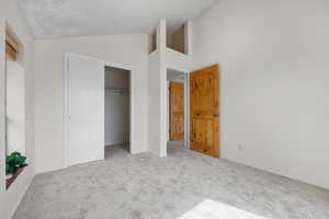 Unfurnished bedroom featuring a closet, light colored carpet, a textured ceiling, and vaulted ceiling