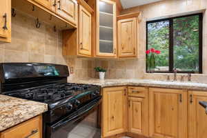 Kitchen featuring tile patterned flooring, light stone counters, sink, and black gas range oven