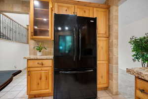 Kitchen with a textured ceiling, light tile patterned floors, light stone countertops, and black fridge