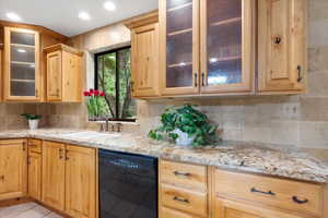 Kitchen with dishwasher, tasteful backsplash, light stone counters, and sink