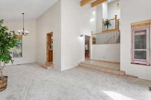 Unfurnished living room with light carpet, high vaulted ceiling, beam ceiling, and a notable chandelier