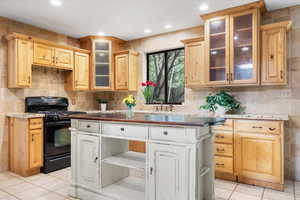 Kitchen with black range, light brown cabinetry, light stone countertops, and light tile patterned flooring