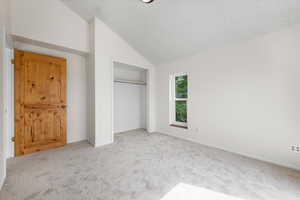 Unfurnished bedroom featuring lofted ceiling, a closet, carpet floors, and a textured ceiling