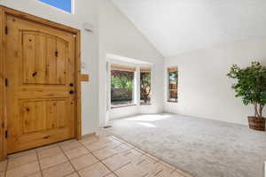 Foyer entrance featuring high vaulted ceiling, light carpet, and a textured ceiling