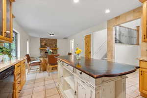 Kitchen with a center island, light tile patterned floors, black dishwasher, and a stone fireplace